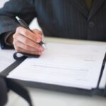 Persona firma un contrato con esfero sobre un escritorio
