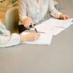Dos mujeres revisan y firman documentos sobre una mesa