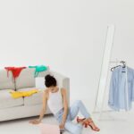 Mujer compra en línea desde su computador portátil, rodeada de ropa