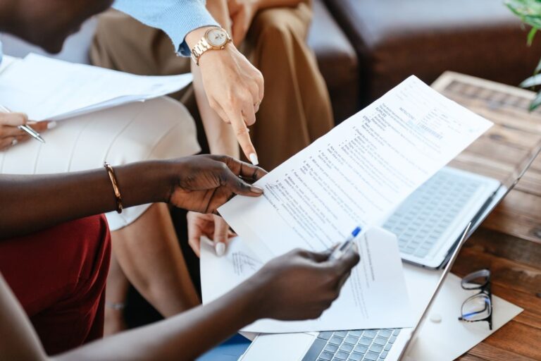 Concepto 016941 del 07-09-2026. Cambiario. Base de la multa por no declarar el dinero en efectivo o los títulos representativos de dinero al ingresar o salir del país. 2 Colegas revisan información en documentos sobre una mesa de oficina