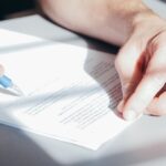Manos firmando un documento con un bolígrafo azul sobre un escritorio