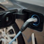 Comunicado de prensa DIAN 127 del 01-10-2026. IVA. Devoluciones por compra de vehículos híbridos y eléctricos. Cable de carga conectado a un vehículo eléctrico